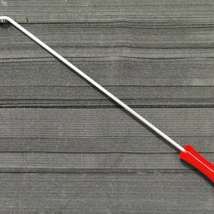 Könnte beinhalten: Ein weißes Metallwerkzeug mit rotem Griff. Das Werkzeug hat einen langen, geraden Schaft, der sich am Ende krümmt. Der rote Griff befindet sich am unteren Ende des Werkzeugs.