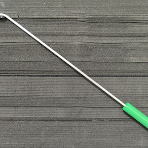 Könnte beinhalten: Ein weißes Metallwerkzeug mit gebogenem Ende und einem hellgrünen Griff. Das Werkzeug befindet sich vor einem dunkelgrauen, strukturierten Hintergrund. Der Griff ist zylindrisch und scheint aus Kunststoff zu sein.