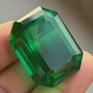 May include: A large, emerald-cut gemstone with a deep green hue. The facets of the gem reflect light, creating a brilliant shine. The rectangular shape and polished surface highlight the clarity and color of the stone.