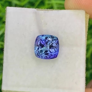 Pu&ograve; includere: Una gemma taglio cuscino con un vibrante colore blu e viola. La gemma &egrave; posta su una superficie bianca, mettendo in risalto le sue sfaccettature e la sua brillantezza. Il colore della pietra passa da un indaco intenso a tonalit&agrave; pi&ugrave; chiare di blu.