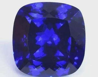 May include: A square-shaped, cushion-cut gemstone in a deep blue hue. The gem features rounded corners and multiple facets that reflect light. The gemstone is set against a white background, highlighting its colour and brilliance.