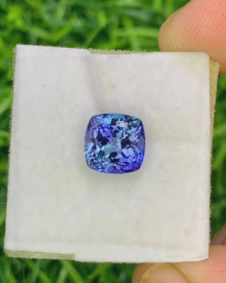 Pu&ograve; includere: Una gemma taglio cuscino con un vibrante colore blu e viola. La gemma &egrave; posta su una superficie bianca, mettendo in risalto le sue sfaccettature e la sua brillantezza. Il colore della pietra passa dall'indaco intenso a tonalit&agrave; pi&ugrave; chiare di blu.