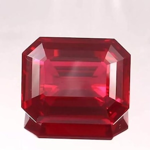 May include: A faceted, rectangular-cut, deep red gemstone with a high degree of clarity. The gem's facets reflect light, creating a brilliant display of color and sparkle. The gemstone is likely a ruby, a popular choice for jewelry.