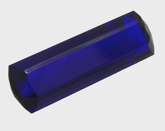 May include: A rectangular, deep blue crystal with multiple facets. The crystal has a polished surface and a slightly curved end. The object is a solid, transparent material, with light reflecting off the facets, creating highlights and shadows.