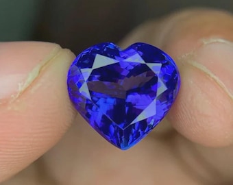 May include: A heart-shaped, deep blue gemstone with a faceted surface. The gem is cut to maximise light reflection, creating a sparkling effect. The stone is held between fingers, highlighting its shape and colour.