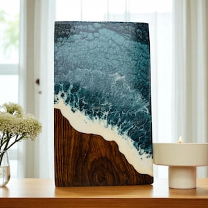 May include: A rectangular wooden art piece with a resin ocean design. The artwork features a dark brown wooden base, a white foamy wave, and a blue and teal ocean design. A candle in a white holder sits nearby.
