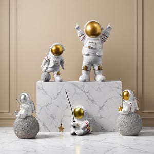 May include: A collection of astronaut figurines in various poses. The figurines are white with gold or silver helmets and accents. Some astronauts are standing, while others are seated on gray moon-shaped bases, holding fishing rods with star-shaped lures.