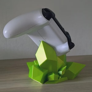 May include: A white and black game controller resting on a bright green geometric stand. The stand is designed to resemble a cluster of stylized crystals. The controller is angled upwards, showcasing its design.