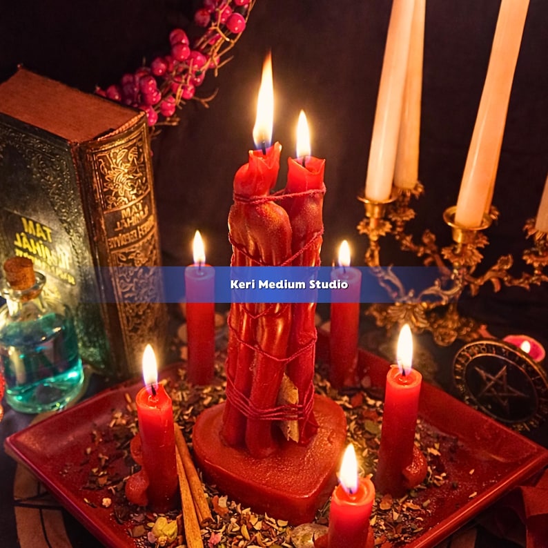 May include: A collection of lit red candles, including a large central candle formation, sit on a red tray. A vintage book, a small bottle, and a decorative candle holder are also present. The image has a mystical or spiritual theme.