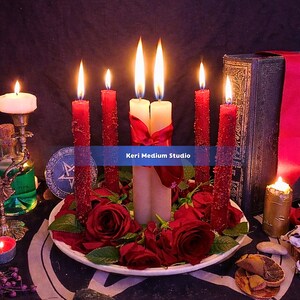 May include: A ceremonial display featuring lit red and white candles, red roses, and a decorative plate. The candles are arranged around a central pair, with a red ribbon. The image includes the text "Keri Medium Studio".