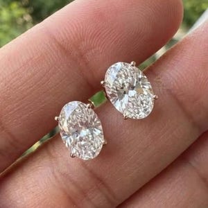 Könnte beinhalten: Ein Paar Ohrstecker mit oval geschliffenen, klaren Steinen in einer Metallfassung. Die Steine zeichnen sich durch hohe Reinheit und Brillanz aus und reflektieren das Licht über die zahlreichen Facetten jedes ovalen Edelsteins.