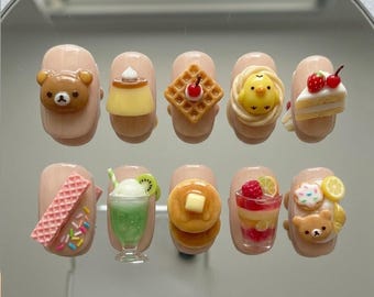 Peut inclure: Dix faux ongles décorés de motifs de desserts miniatures. Chaque ongle présente un aliment miniature différent, notamment un ours, un pudding, une gaufre, un poussin, un gâteau, une gaufrette, un smoothie, des crêpes, un parfait et un beignet.