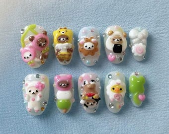 May include: A set of ten artificial nails, each adorned with a unique, colorful, cartoon-style character design. The designs include bears, lions, and other cute figures, with accents of rhinestones and hearts. The nails are oval-shaped and set against a light blue background.