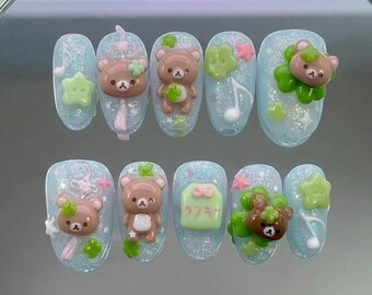 May include: A set of ten artificial nails with a light blue glitter base. Each nail features 3D bear and star designs in brown, green, and pink. Some nails have musical notes and Japanese text.