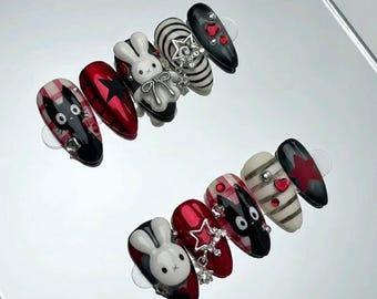May include: A set of almond-shaped, press-on nails with various designs. The nails feature a white bunny, red stars, black and white stripes, and cartoon cat faces. Some nails have gem accents.