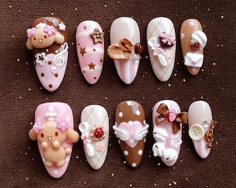May include: A collection of ten almond-shaped, decorated artificial nails. Each nail features a unique design with pink, brown, and white colors, adorned with 3D embellishments like hearts, bows, and cartoon characters. Some nails have musical notes and stars.