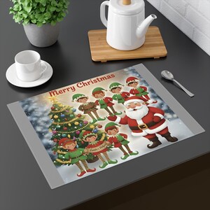 May include: A rectangular placemat with a Christmas theme. The design features Santa Claus, elves, and a decorated Christmas tree. The words "Merry Christmas" are printed at the top. The placemat has a gray border.