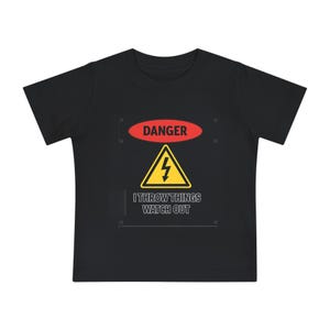 Peut inclure: T-shirt noir avec un motif graphique. Le motif comprend un ovale rouge avec le mot "DANGER", un triangle jaune avec un éclair et le texte "I THROW THINGS WATCH OUT".