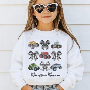 May include: White sweatshirt featuring colorful monster trucks and checkered bows. The text "Monster Mama" is printed below the graphics. The sweatshirt is from "Tiny Baby Love".