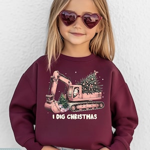 Peut inclure: Sweat-shirt bordeaux avec un dessin d'une excavatrice rose avec un sapin de Noël et le Père Noël. Le texte "I DIG CHRISTMAS" est imprimé en dessous. La marque "Tiny Baby Love" est imprimée en haut.