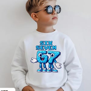 May include: White sweatshirt with the text "SIX SEVEN" in blue pixelated font, featuring animated blue numbers with faces. The sweatshirt is labeled "WHITE" at the bottom.