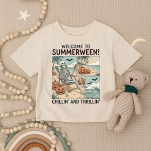 May include: A cream-colored short-sleeve t-shirt featuring a graphic print with the text "WELCOME TO SUMMERWEEN!" and "CHILLIN' AND THRILLIN'". The illustration depicts a skeleton sitting in a beach chair surrounded by jack-o'-lanterns.