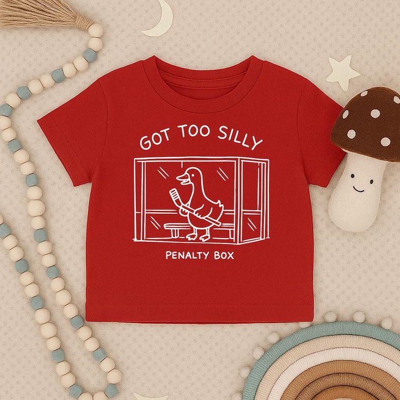 May include: A red short-sleeved t-shirt featuring a white line drawing of a duck holding a hockey stick inside a penalty box. The text above the graphic reads GOT TOO SILLY and the text below the graphic reads PENALTY BOX in white lettering.