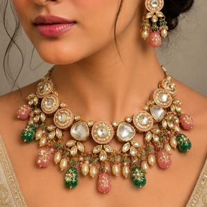 May include: A gold-toned necklace and matching earrings set. The necklace features pink and green gemstone drops, clear stones, and pearl accents. The earrings mirror the necklace design. The jewelry is set against a neutral background.