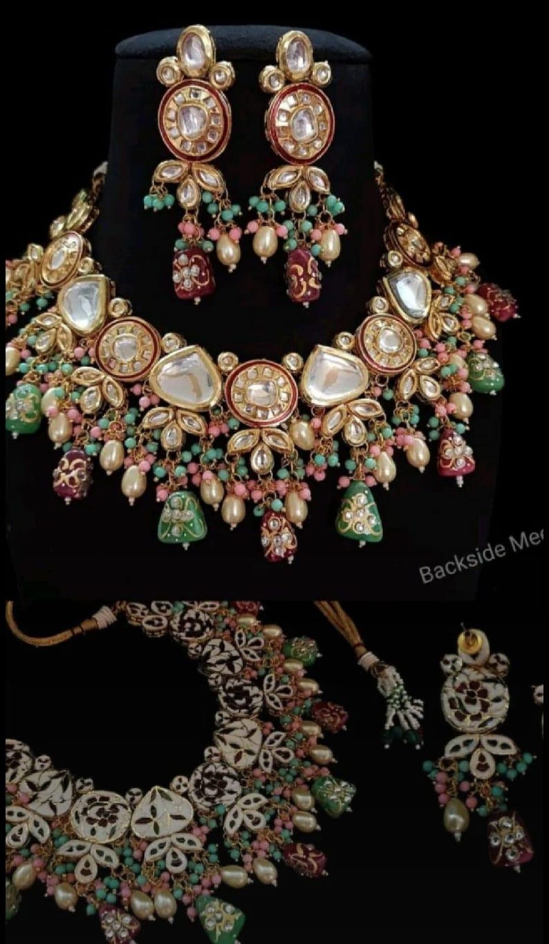 May include: A gold-toned necklace and earring set with clear and red accents, pearls, and colorful beads. The necklace features large, clear stones and intricate floral designs. The earrings mirror the necklace's design, creating a cohesive look.