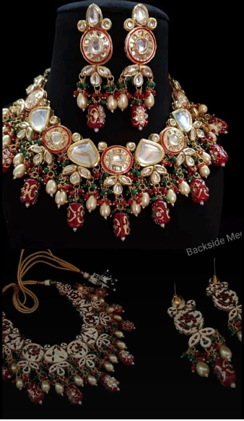 May include: An ornate jewelry set featuring a necklace and matching earrings. The necklace and earrings are gold-toned with red, green, and white accents, and dangling pearl-like beads. The set is displayed against a black background.