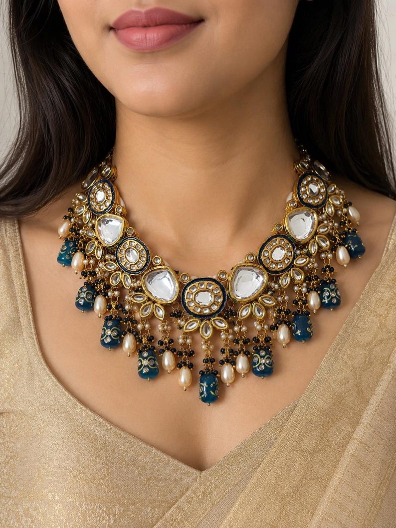 May include: A gold-toned statement necklace with large, clear, oval-shaped stones and smaller, round, black and white stones. The necklace features dangling blue and gold accents and white pearls, creating an elegant and ornate design.