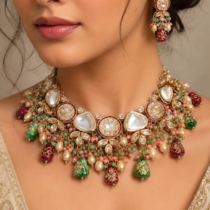 May include: A gold-toned necklace and matching earrings set. The necklace features large, clear, and red-rimmed circular and teardrop-shaped pendants, accented with green and pink beads, and white pearls. The earrings mirror the necklace design.