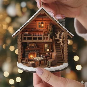 Pode incluir: Enfeite de Natal em miniatura detalhado em forma de cabana de madeira. A cabana de dois andares apresenta uma lareira, um sótão e uma escada. O exterior é feito de toras marrons com um telhado nevado. No interior, uma lareira acesa e uma pequena mesa.