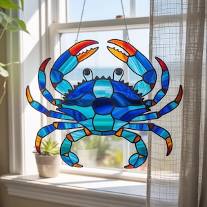 Pode incluir: Decoração de caranguejo em vitral com um corpo azul vibrante, acentuado com pinças e pernas laranja e vermelhas. O caranguejo é suspenso por uma corrente, perfeito para uma janela ou parede. O design do caranguejo apresenta um mosaico de peças de vidro.
