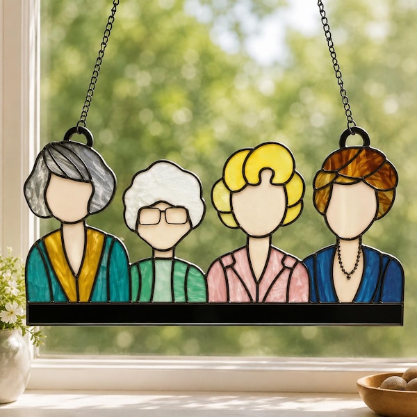 May include: A stained glass suncatcher featuring four stylized figures with distinct hair colors and clothing styles, including teal, green, pink, and blue outfits. The piece is suspended by two black metal chains and has a solid black base.