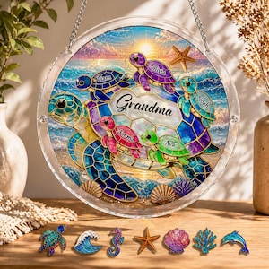 May include: A round, clear glass wall hanging featuring a colorful sea turtle design. The design includes the word "Grandma" and the names Liam, Olivia, Noah, Emma, and Ava. The background depicts a sunset over the ocean, with additional sea-themed embellishments.