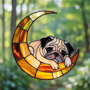 May include: Stained glass crescent moon with a sleeping pug dog. The moon is composed of amber, gold, and brown glass pieces. The pug has a tan and black coat, with a sleepy expression. A decorative suncatcher.