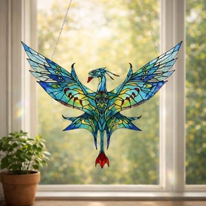 May include: Stained glass art piece depicting a stylized bird with outstretched wings. The bird features a vibrant color palette of blues, greens, and yellows, with red accents. The artwork is suspended by a chain, suitable for window display.