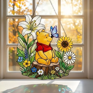 May include: Stained glass window art depicting a yellow bear in a red shirt seated on a tree stump, with a blue butterfly on its nose. The art includes white lilies, a sunflower, daisies, and other colourful flowers.