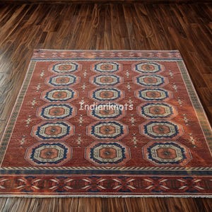 May include: A rectangular, red rug with a repeating geometric pattern. The pattern features octagonal shapes in shades of orange, blue, and cream. The rug has a border with a repeating geometric design and the text "Indianknots".