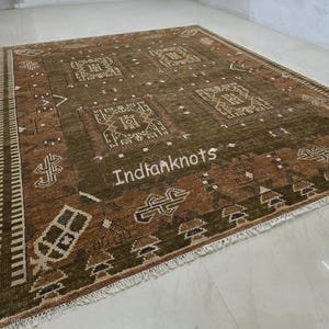 May include: A rectangular, olive green rug with a repeating geometric pattern in shades of brown and beige. The rug has a fringe along the edges and the text "Indianknots" is visible on the rug.