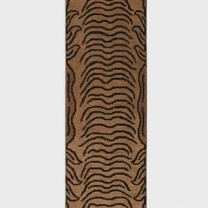 May include: A rectangular runner rug featuring a tan base color with a repeating black tiger stripe pattern across the center. The rug is framed by a decorative black border with a continuous looping design and has short fringe at both ends.