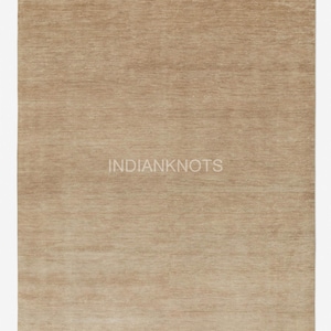 May include: A rectangular, beige rug with a textured surface. The rug has a simple design and the text "INDIANKNOTS" is printed in the center. The rug is suitable for living rooms, bedrooms, or entryways.