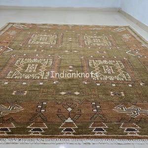 May include: A rectangular olive green and brown rug with intricate geometric patterns. The rug features repeating square and rectangular designs in shades of brown and white, with a fringe border. The text "Indianknots" is visible on the rug.