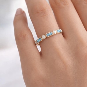 May include: A gold ring featuring alternating rectangular blue and round white gemstones. The ring is set with a delicate beaded edge. The ring is shown on a person's finger.