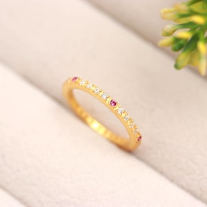 Peut inclure: Une fine bague en or avec une série de petites pierres blanches transparentes alternant avec des pierres roses vives serties sur la moitié supérieure de l'anneau métallique. La bague présente une finition en or jaune poli et un profil fin.