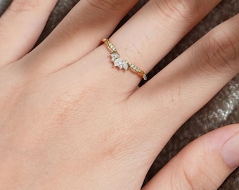 Puede incluir: Un anillo dorado con un diseño curvo, con pequeñas piedras preciosas transparentes y un grupo de piedras más grandes en forma de pétalo en el centro. El anillo se lleva en un dedo, mostrando sus delicados detalles y su elegante estilo.
