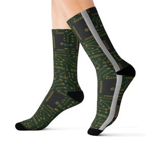 May include: A pair of crew socks featuring a dark green circuit board pattern with gold-colored lines and integrated chip graphics. The design includes black heels and toes, with a vertical light gray stripe running down the side of each sock.