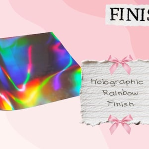 May include: A roll of holographic rainbow foil with a vibrant, iridescent finish. The image also includes a notepad with the text "Holographic Rainbow Finish" and the word "FINISHES" at the top.