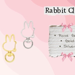 May include: Three metal rabbit-shaped clasps in rose gold, gold, and silver. The clasps have a swivel base and a ring for attaching to items. Text on a paper reads "Rabbit Clasp" and lists color options: Rose Gold, Gold, and Silver.